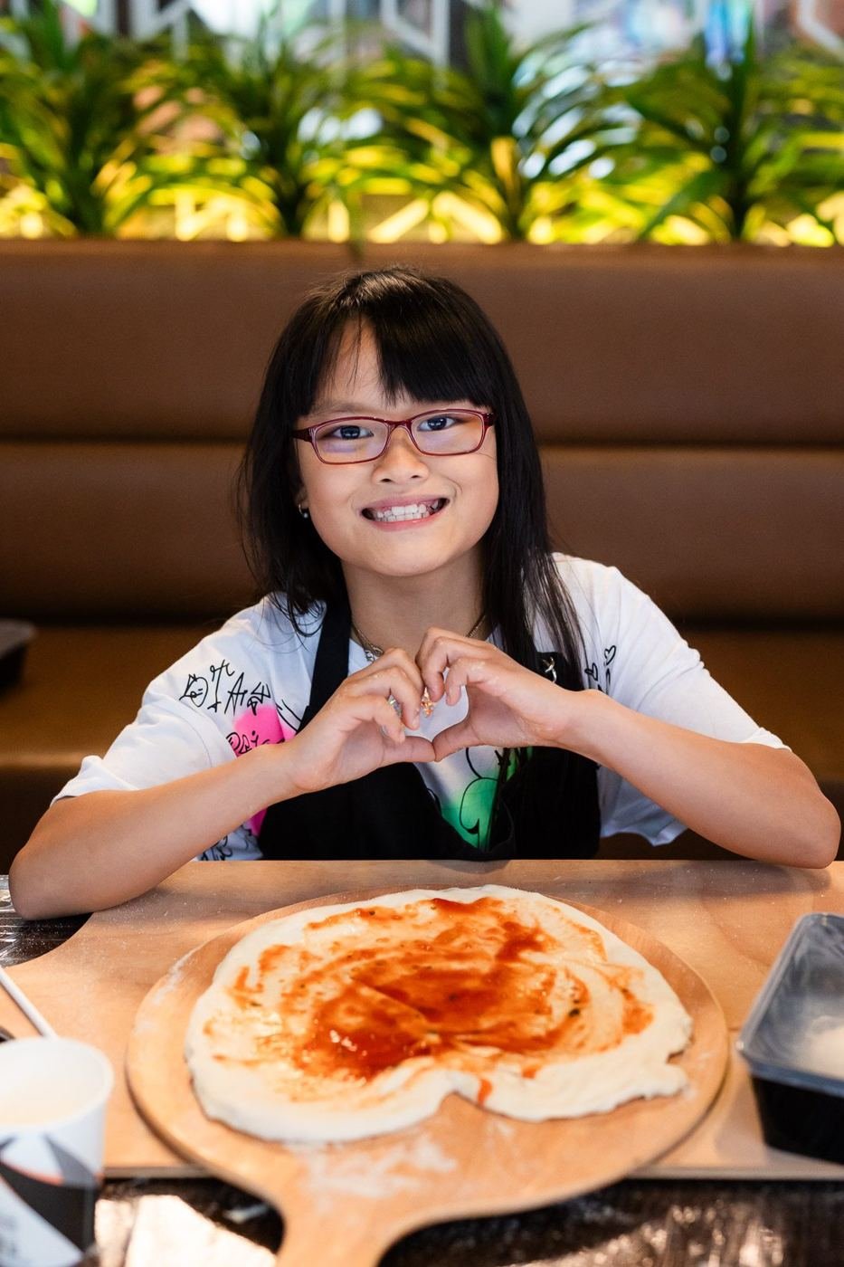 A girl making a heart with her hands over the pizza she made